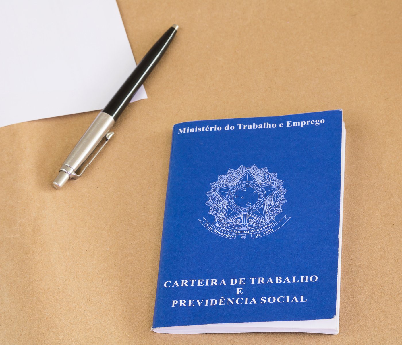 A portfolio of Brazilian workers (Translation 'Labor Permit, Ministry of Labor and Social Security Brazil CTPS'), pen and paper. Brown envelope background.